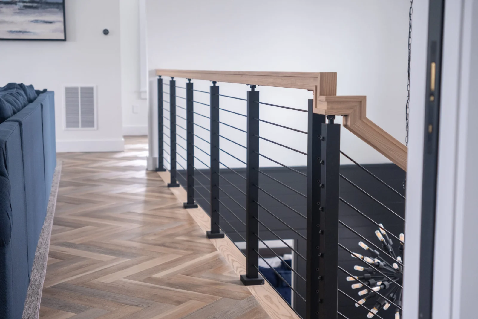 Balcony run of rod railing with wood top rail above a herringbone floor
