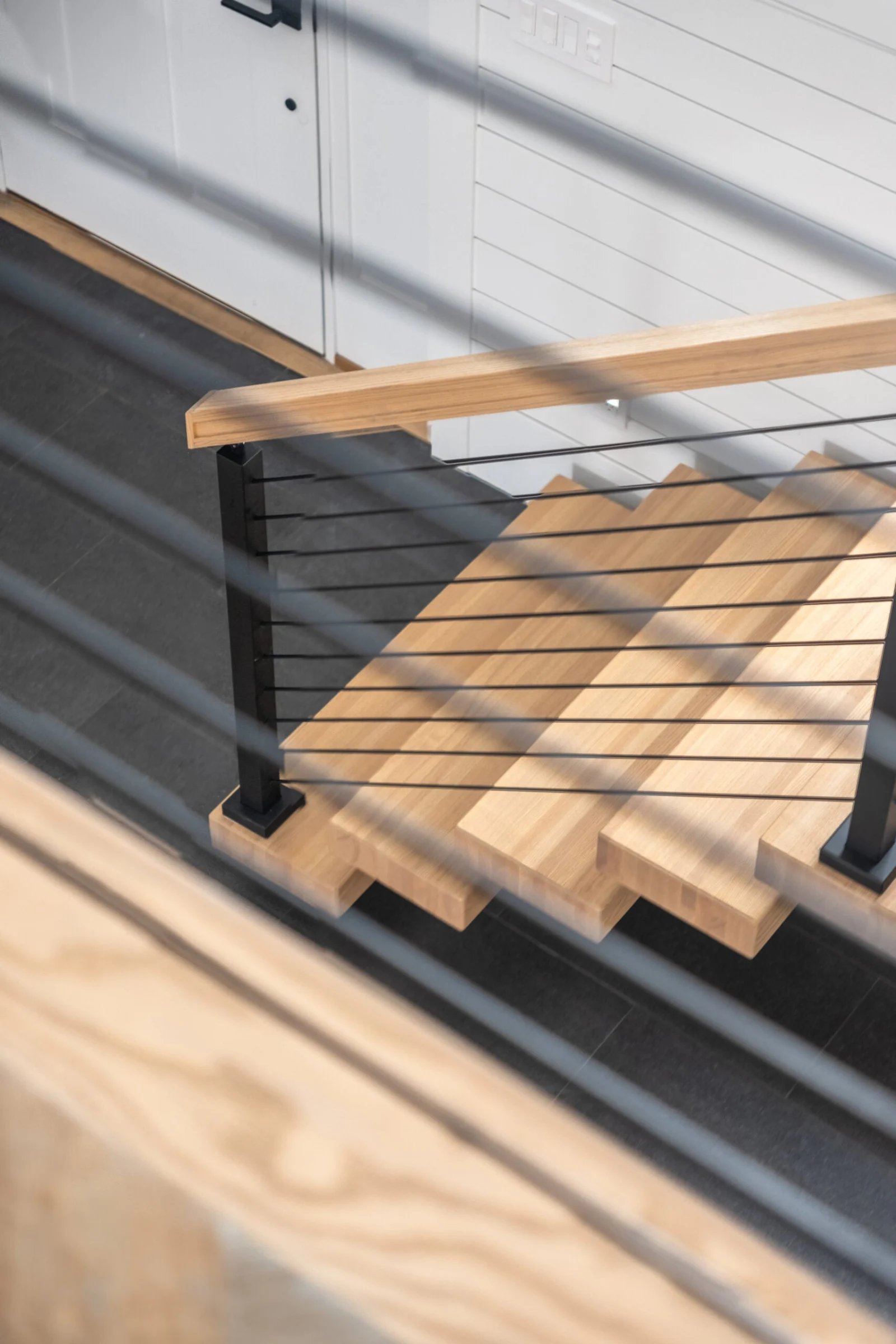 Down-angle on a wood tread and dark rod infill catching striped sunlight