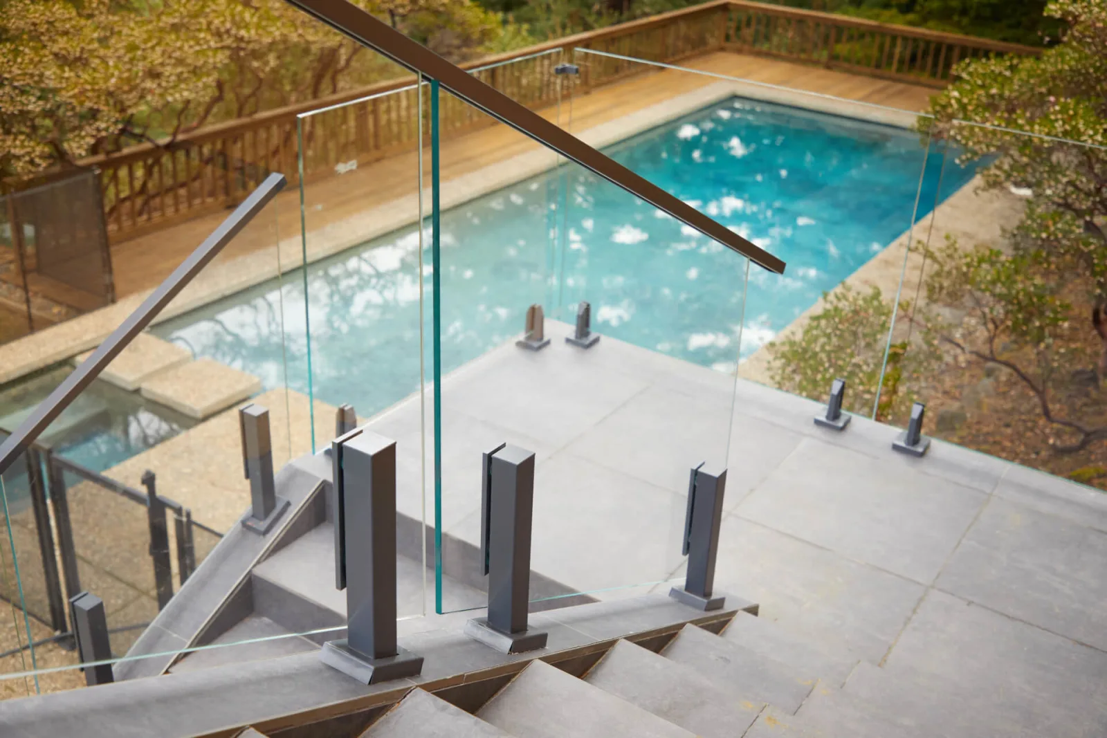 Glass railing and metal handrail at the top of stone steps overlooking a pool