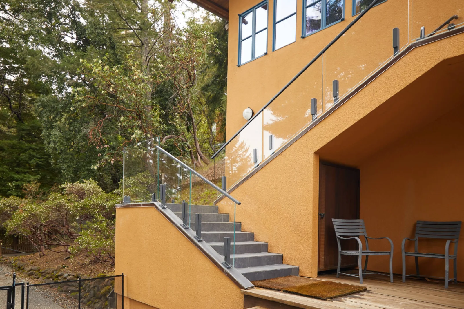 Stone steps beside the house with glass railing and a slim wall-mounted handrail