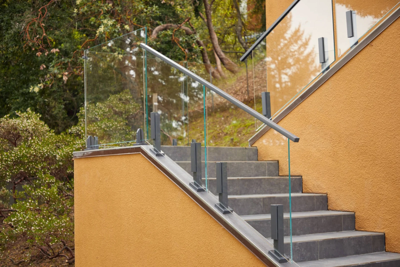 Glass railing and handrail running up outdoor steps against orange stucco