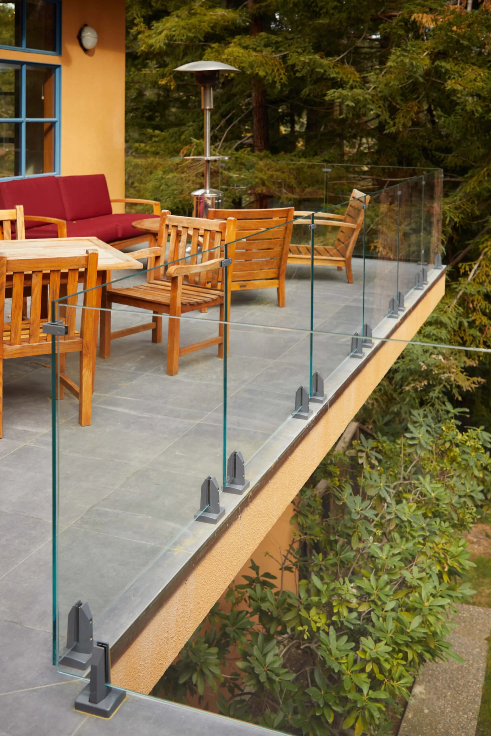 Glass railing on base clamps running along the edge of a stone dining terrace