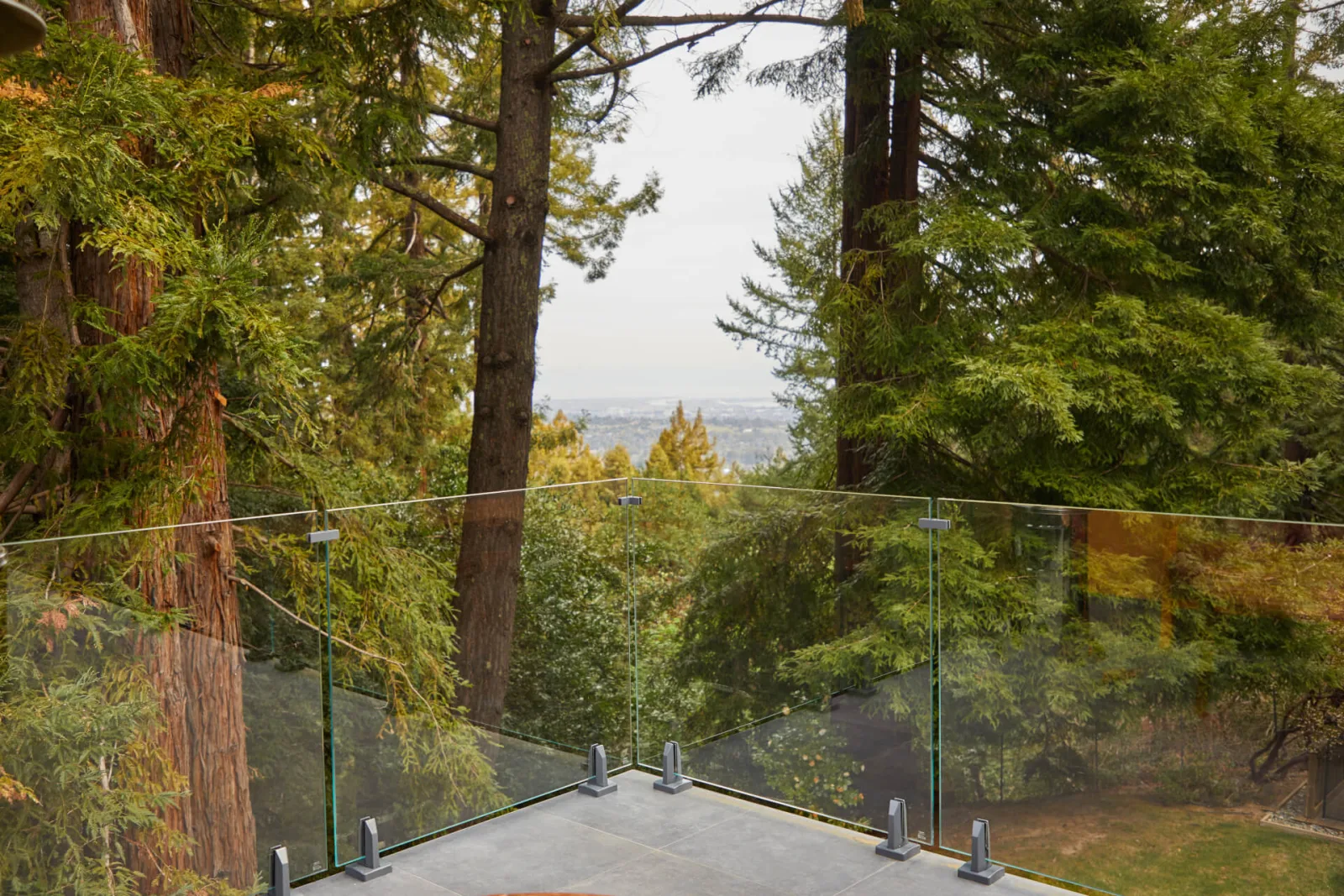 Frameless glass railing along a stone terrace with redwoods and a distant valley view