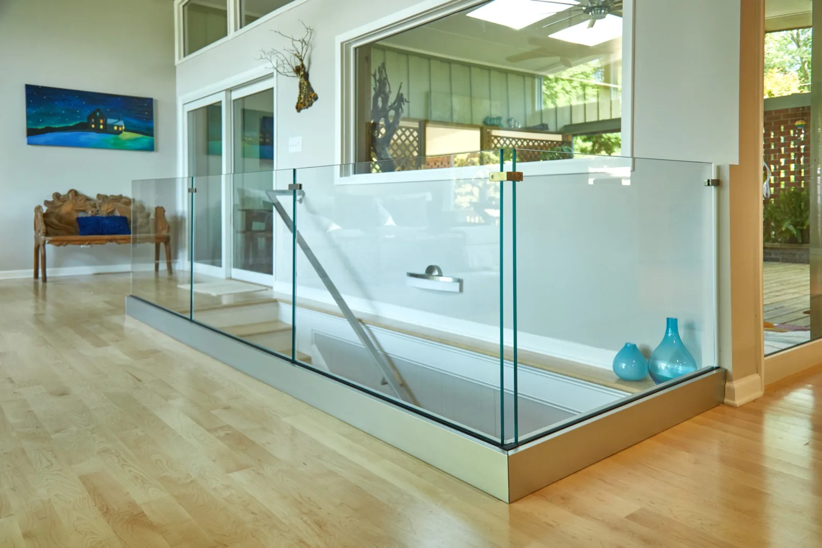Glass railing set in a low base rail enclosing a floor opening in an open room