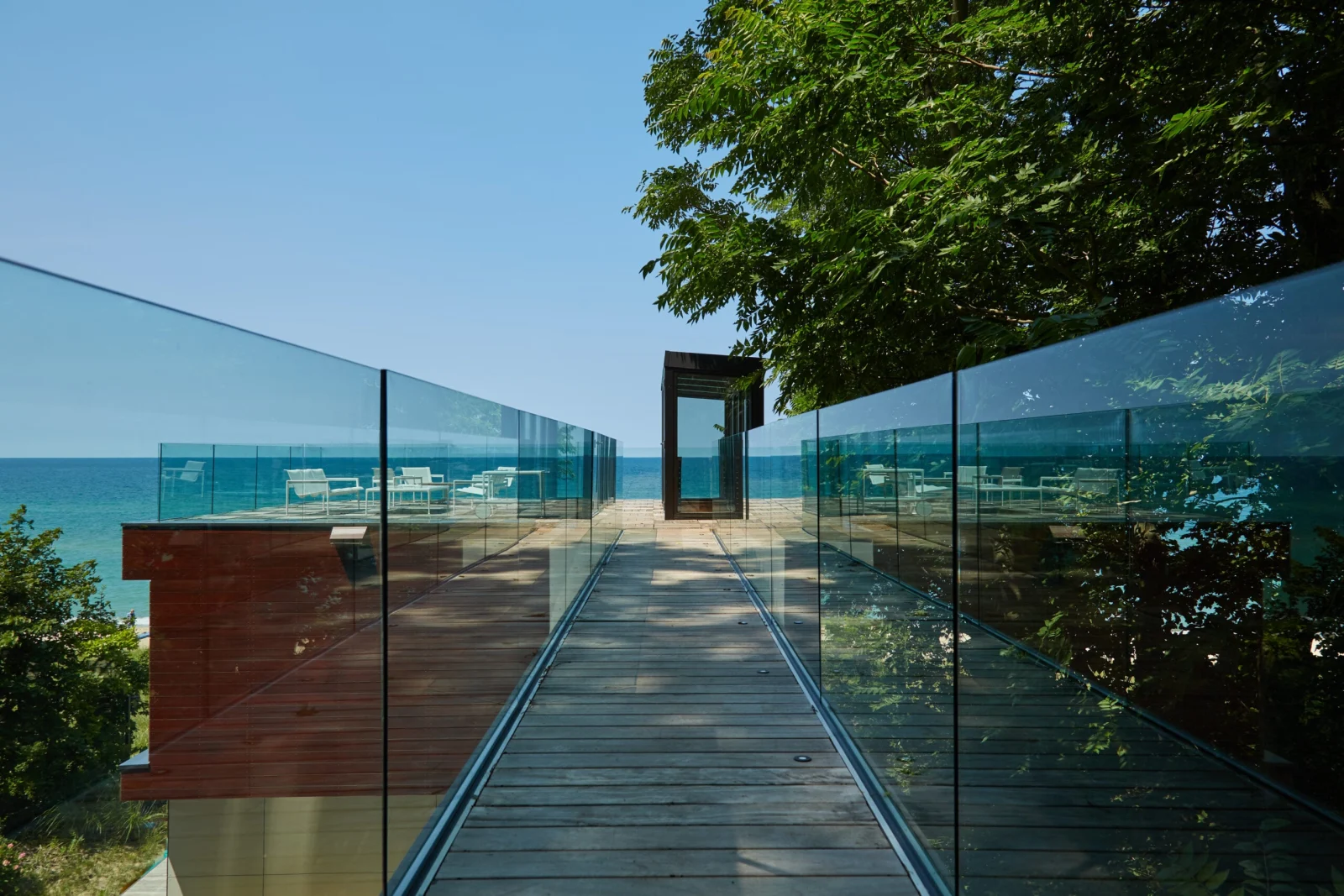 Glass railing lining both sides of a wood walkway toward the lake