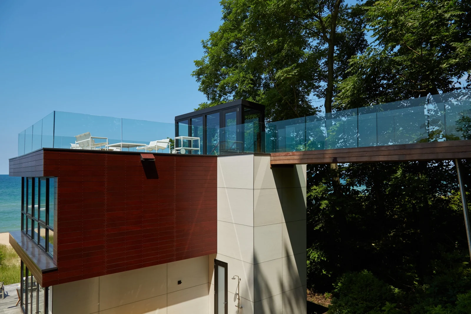 Glass railing on the roof terrace and connecting walkway seen from among the trees