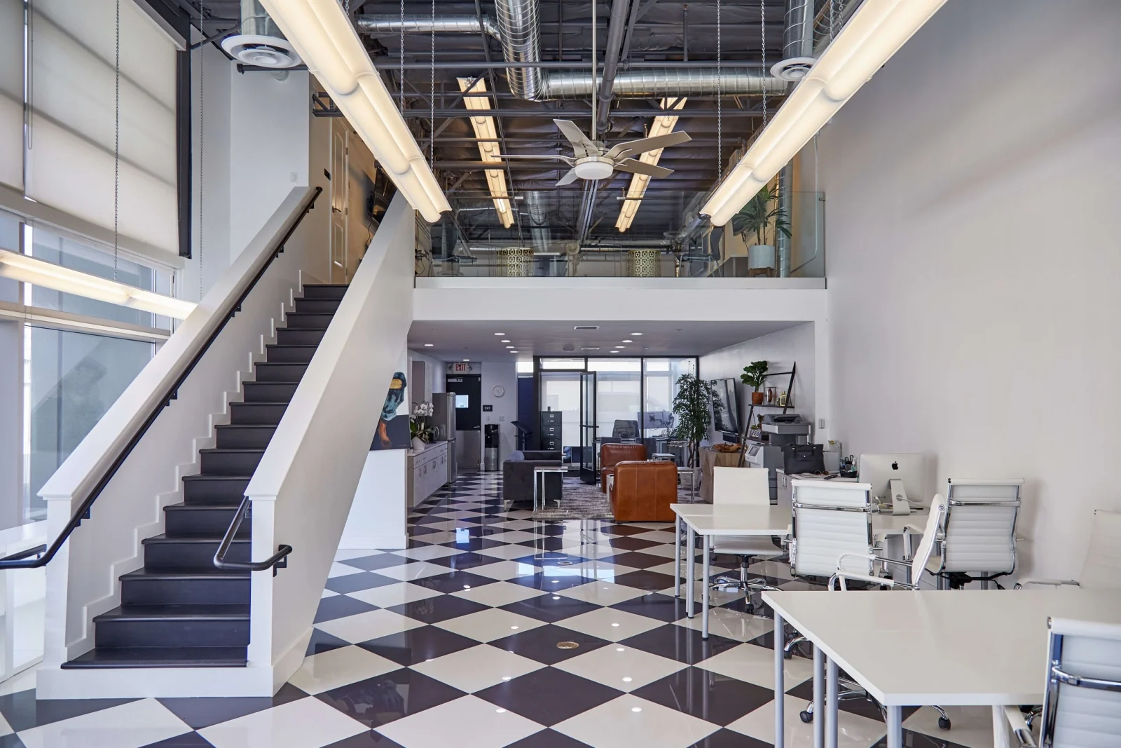 Open office with a dark stair rising to the mezzanine and its glass railing