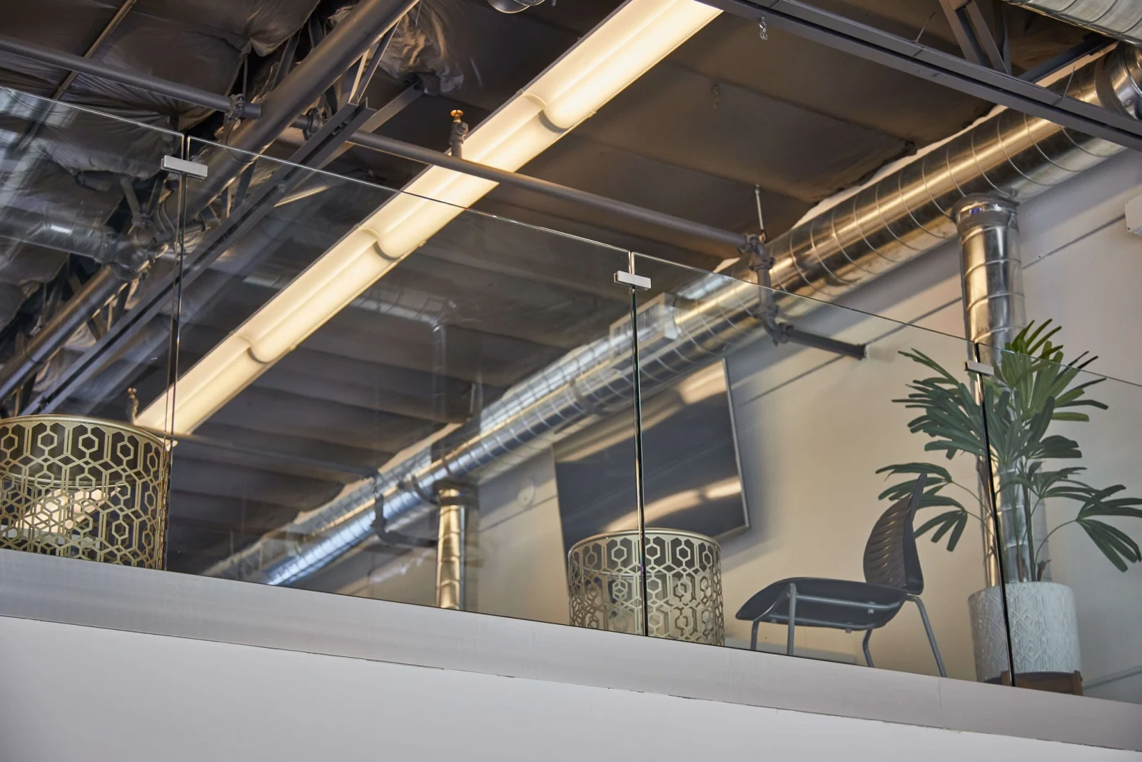 Glass railing seen from the mezzanine floor against ducts and pendant lighting
