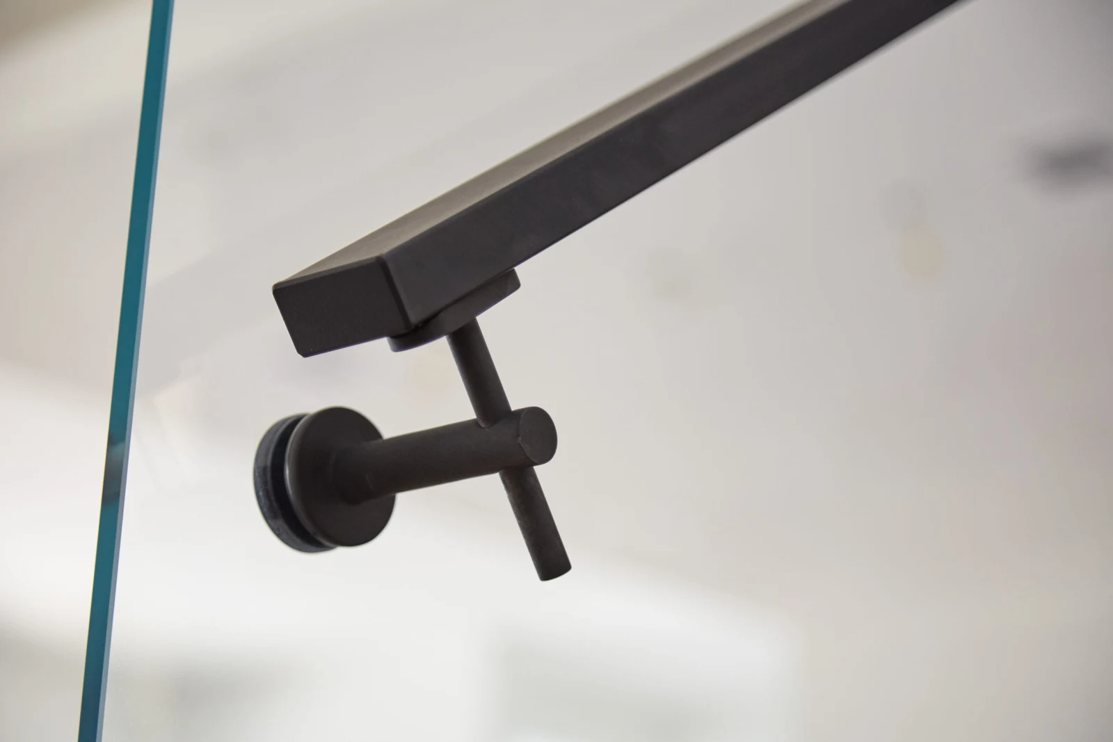 Close view of a black square handrail on a round wall bracket beside glass