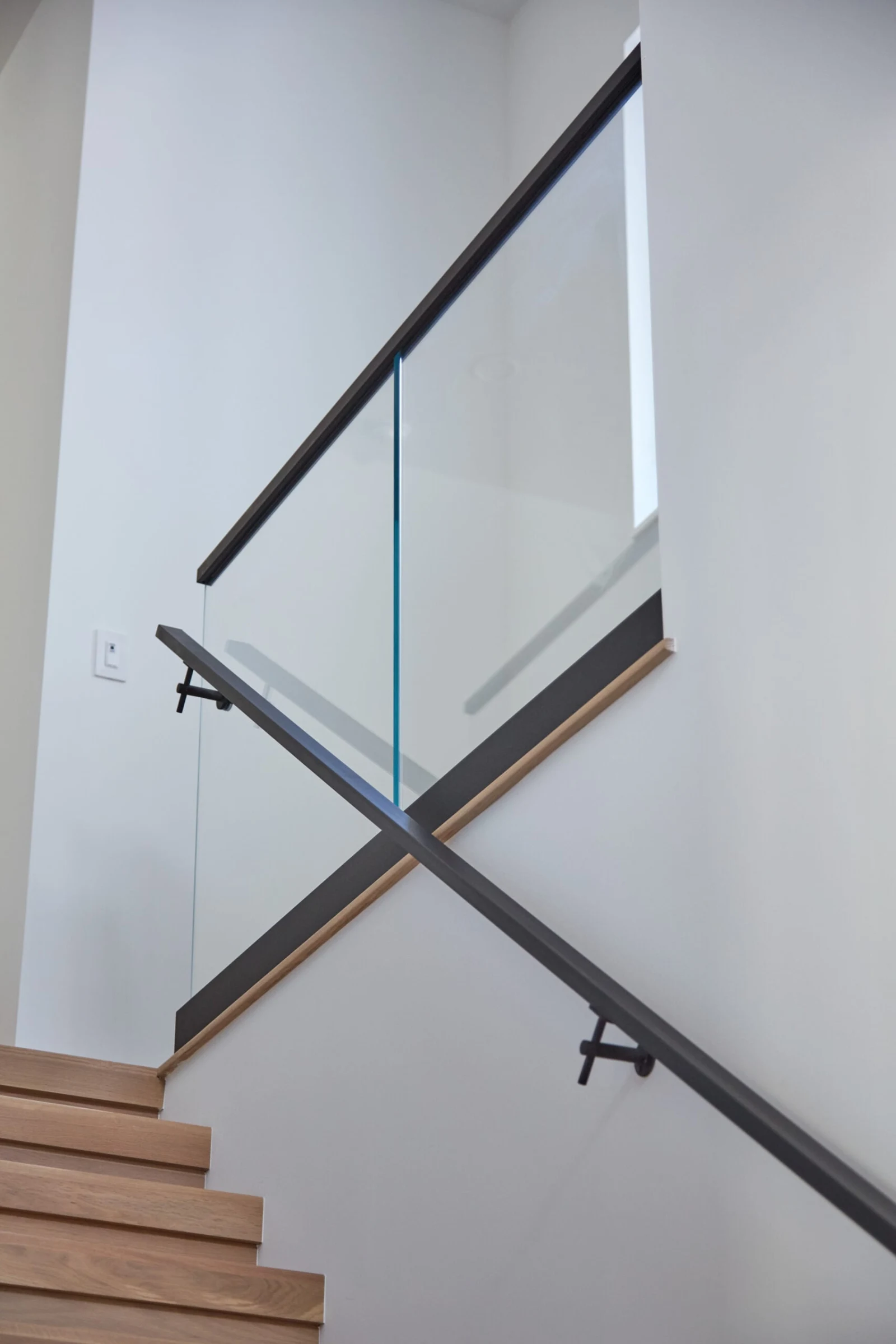 Stair glass railing with black cap rail and a wall-mounted handrail alongside