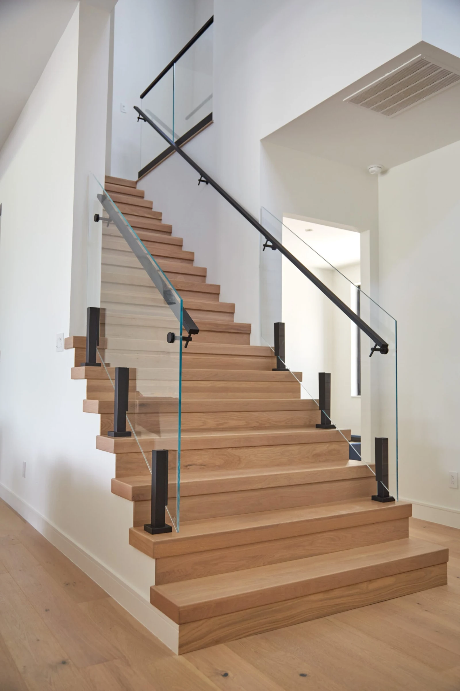 Closed-riser wood stair with black glass clamps, clear panels and a black handrail on standoffs