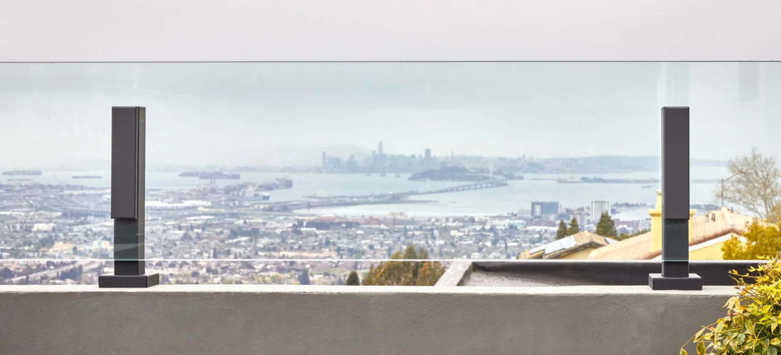Two black posts clamping one glass panel along a concrete parapet above the bay