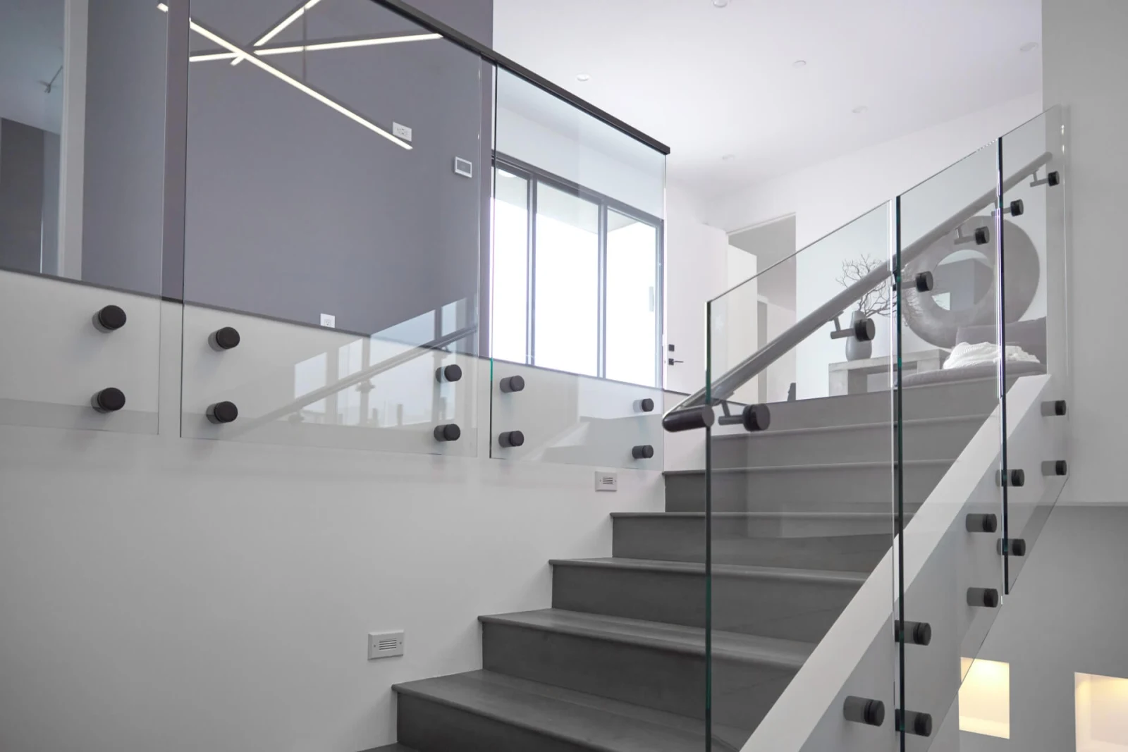 View up the stair past glass panels set in black standoffs below a linear light