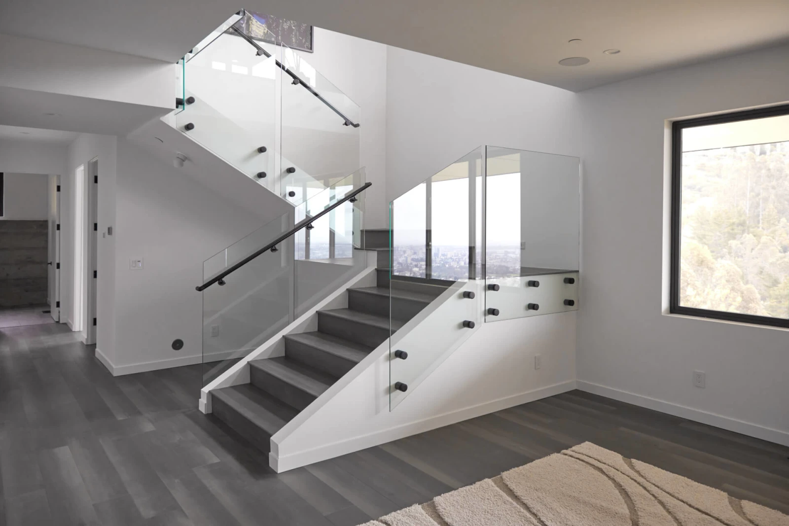 White interior stair and landing enclosed by glass panels with a slim black handrail