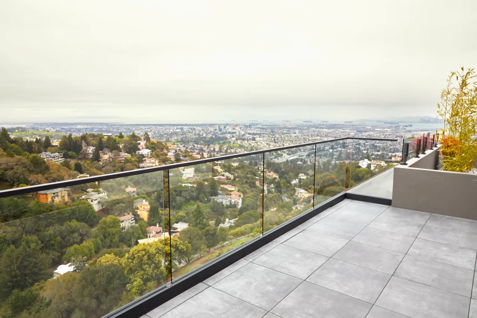 Paver terrace edged by a long glass run with black top rail over hillside homes