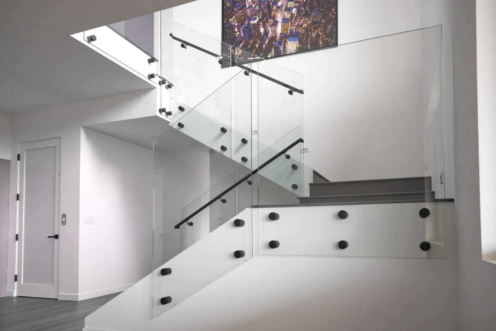 Switchback stair wrapped in glass panels held by black standoff pins with matching black handrails