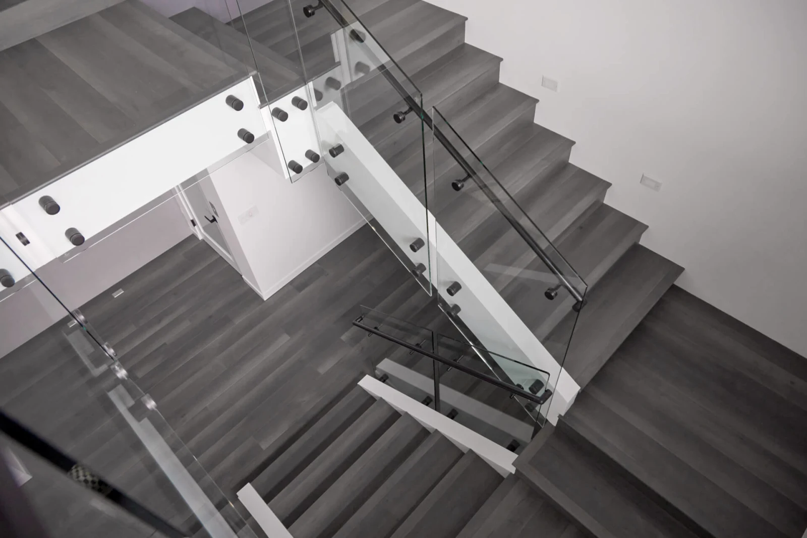 Looking down a stairwell where glass panels on black clamps follow the treads
