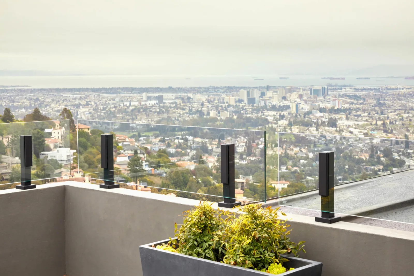 Glass panels in black posts top a stucco parapet behind a planter of greenery