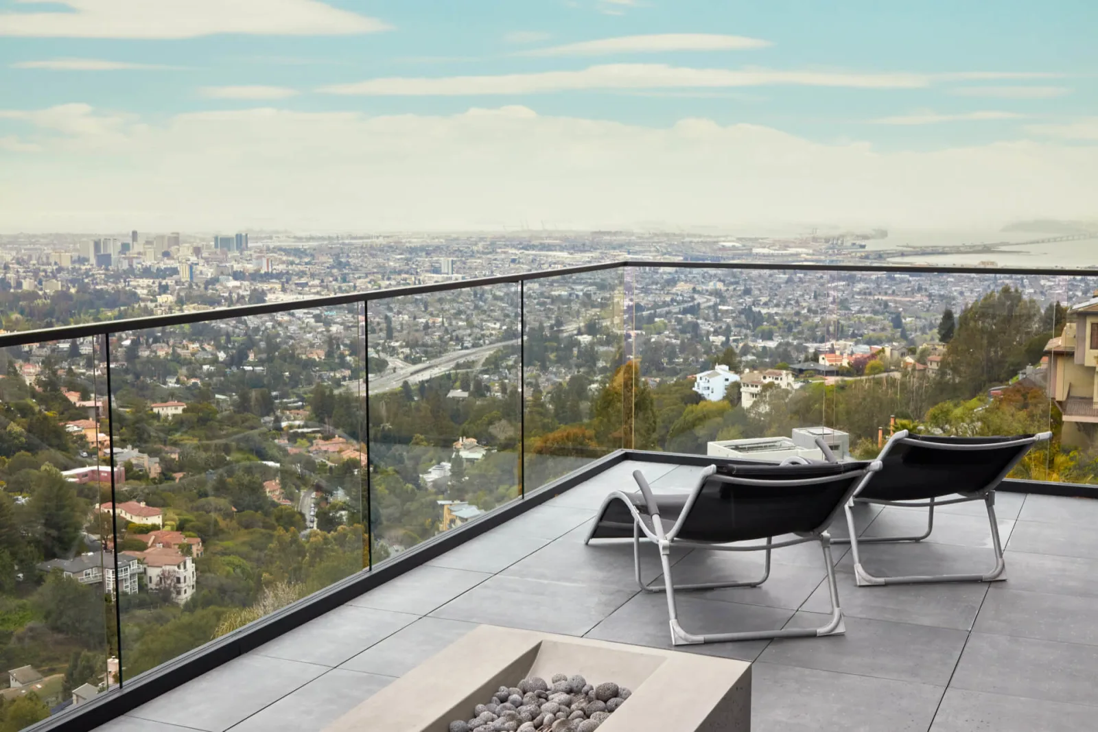 Rooftop terrace ringed by glass railing on black posts above a sweeping city view