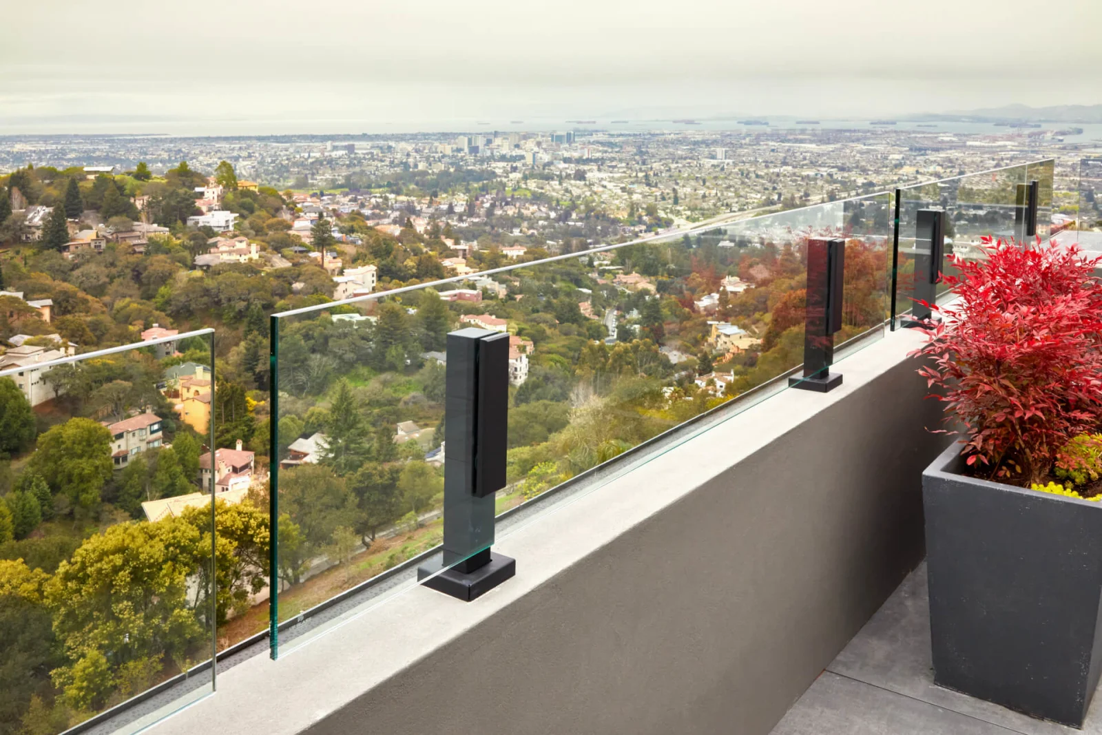 Black base posts and glass panels line a narrow balcony beside a red planting