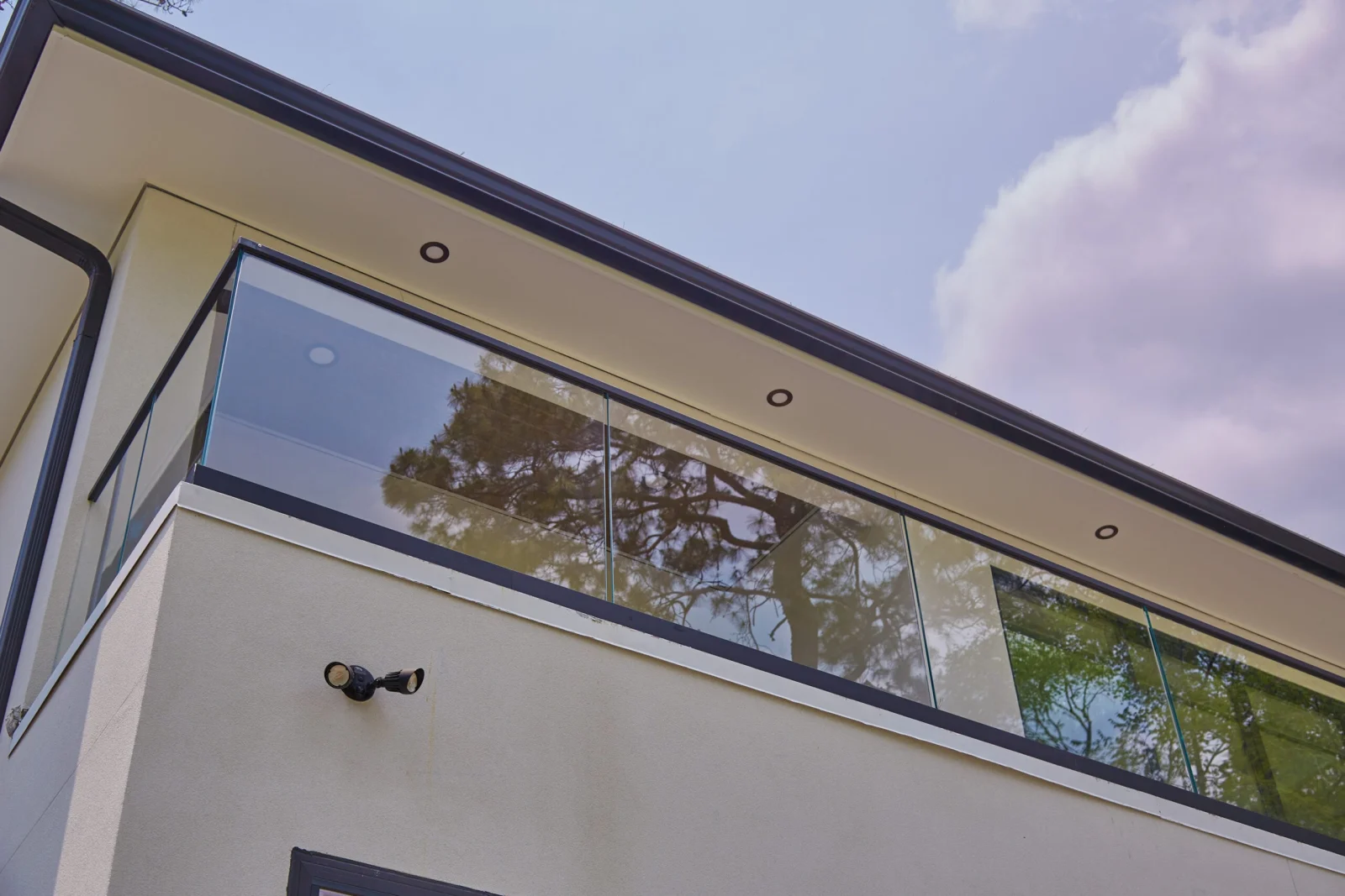Upward view along a glass balcony rail set under a deep roof overhang