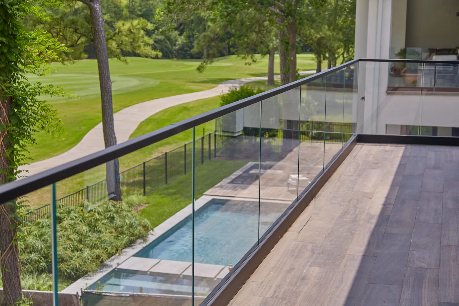 Balcony glass railing with black cap rail overlooking a narrow pool and a green fairway
