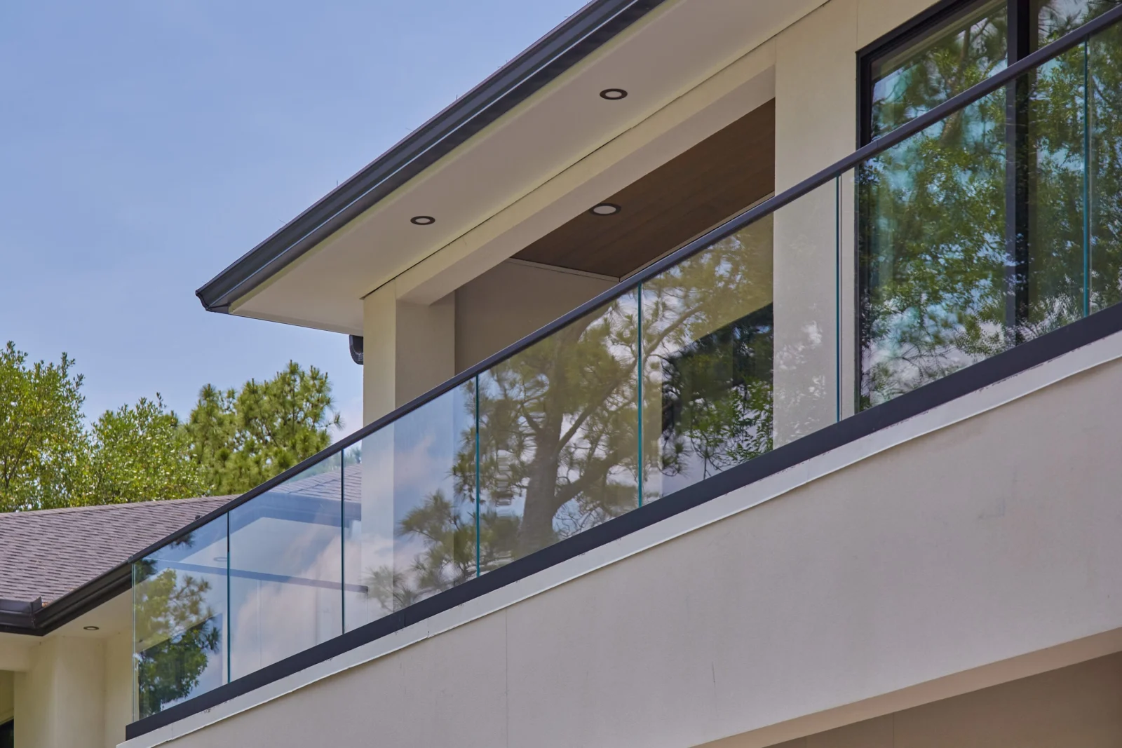 Second-floor balcony glass railing seen from the yard against a clear blue sky