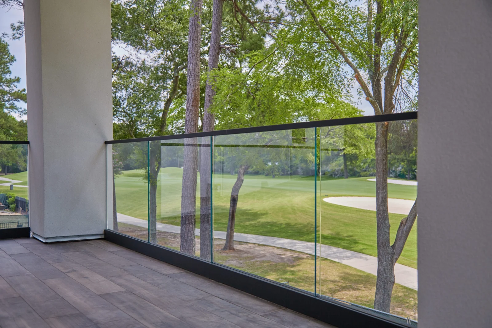 Glass panels between black top and base rails along a plank-floored balcony corner