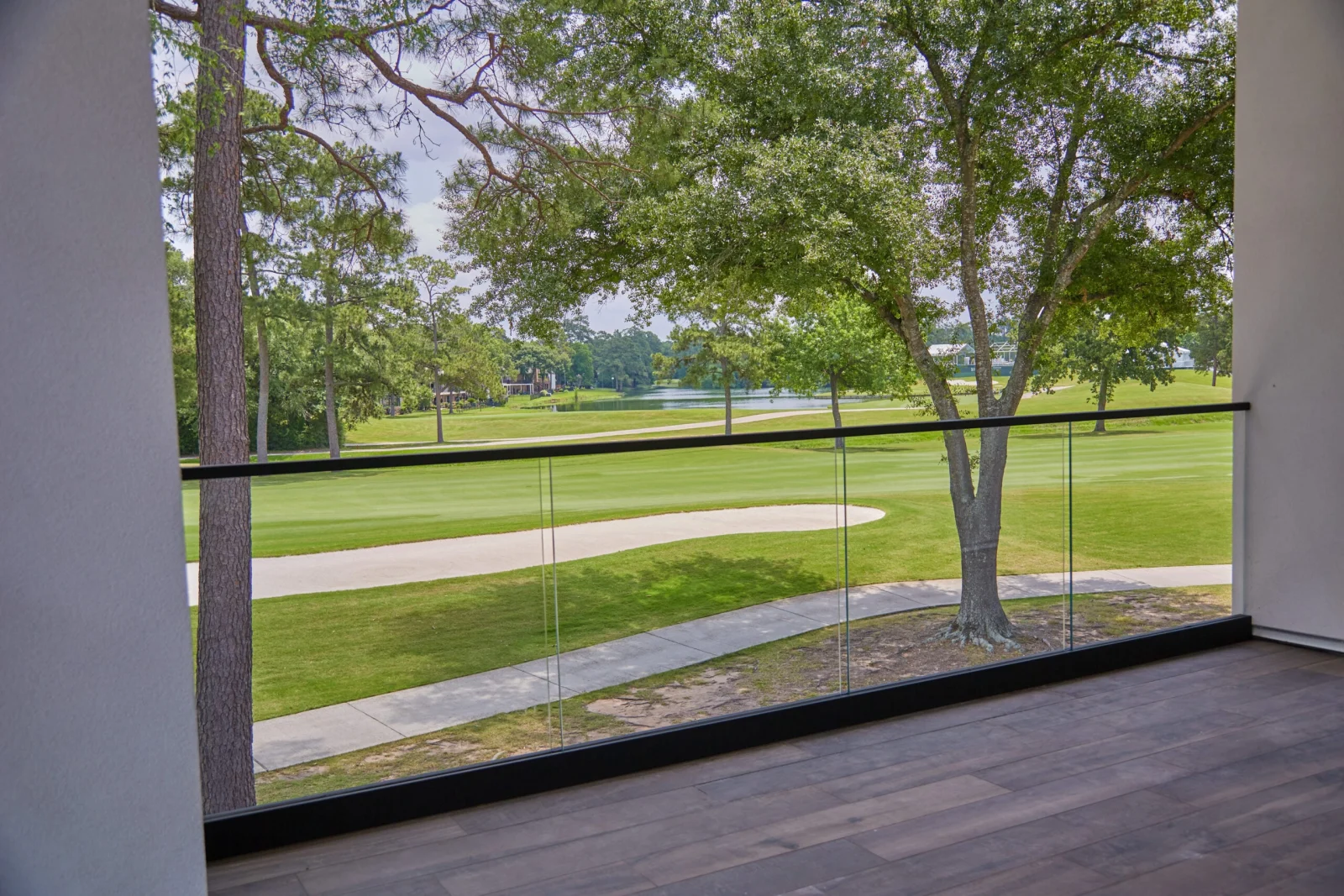 Covered balcony with black-framed glass railing overlooking a golf green and trees