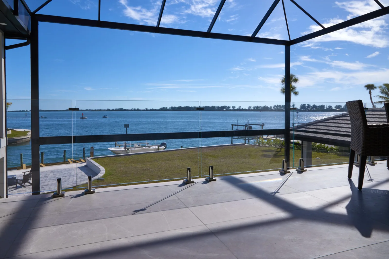Screened waterfront lanai with frameless glass railing and stainless posts facing open bay