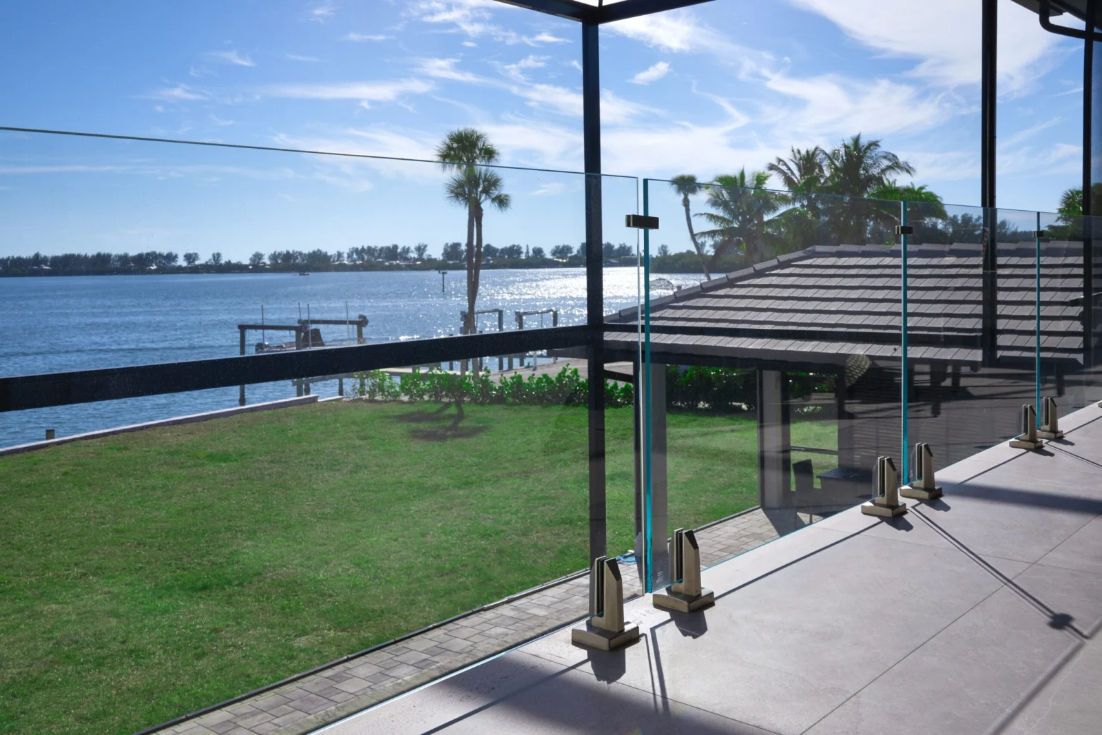 Patio glass railing above a lawn, dock and open bay beyond the panels