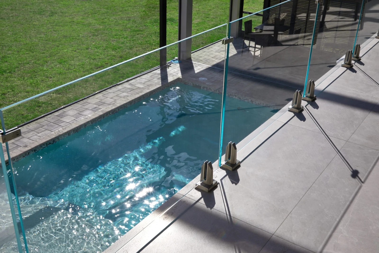 Overhead view of glass pool fencing anchored by stainless spigots on concrete