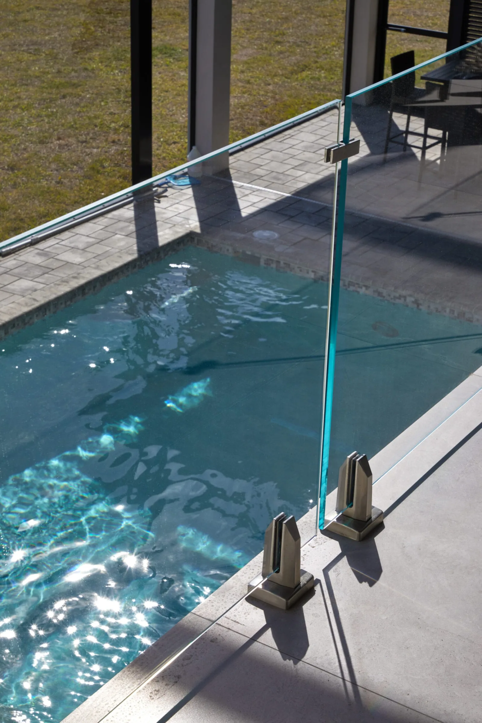 Glass panel on stainless base clamps running beside a sunlit swimming pool
