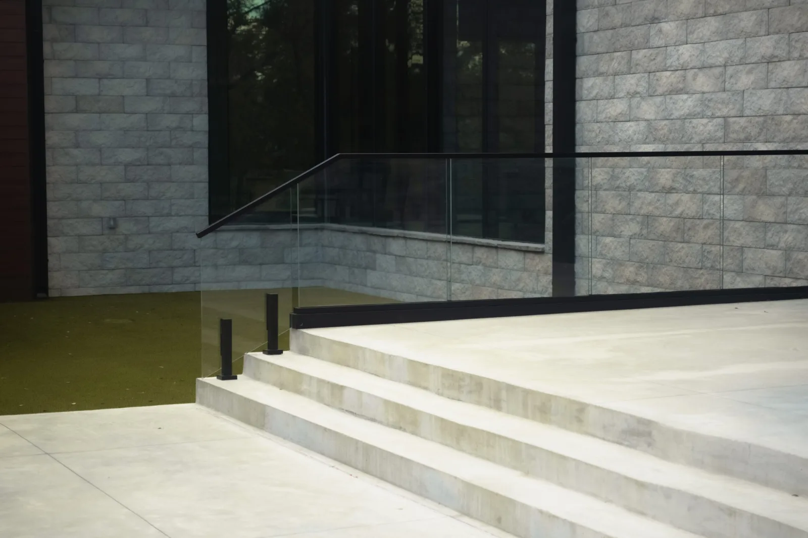 Broad concrete steps meet a glass railing set against a stacked stone wall