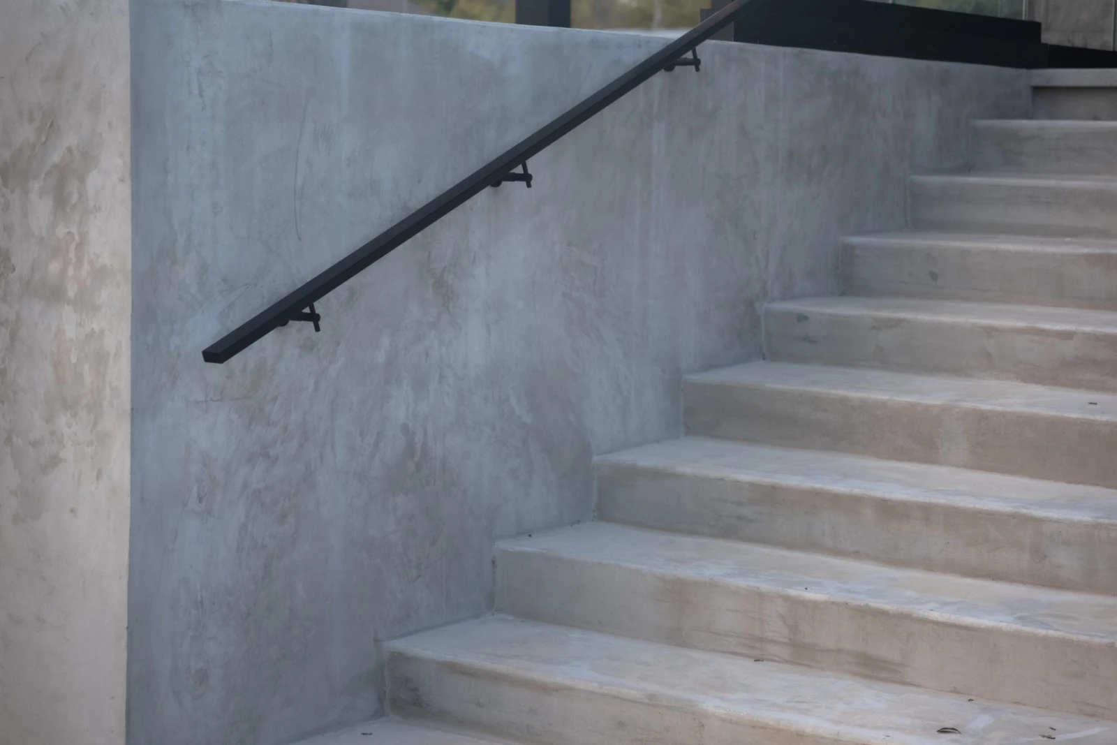 Black wall-mounted handrail follows concrete steps up a smooth plaster garden wall