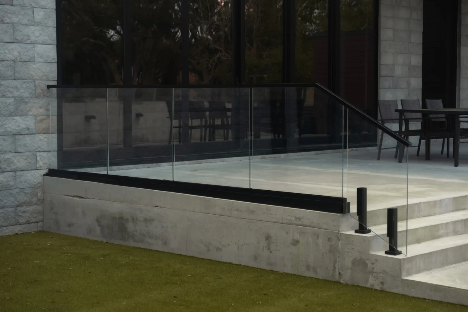 Terrace glass railing on a black base rail with stone walls and patio seating