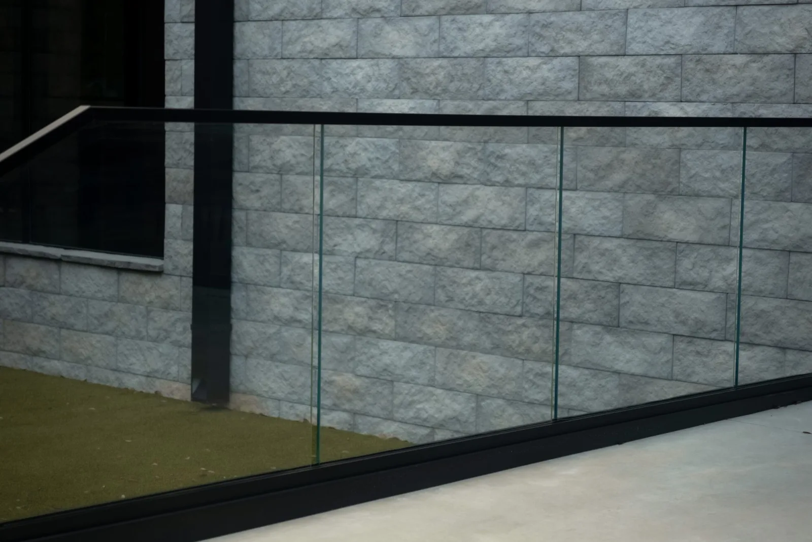 Glass panels and black rail edge a walkway beside a stone block wall