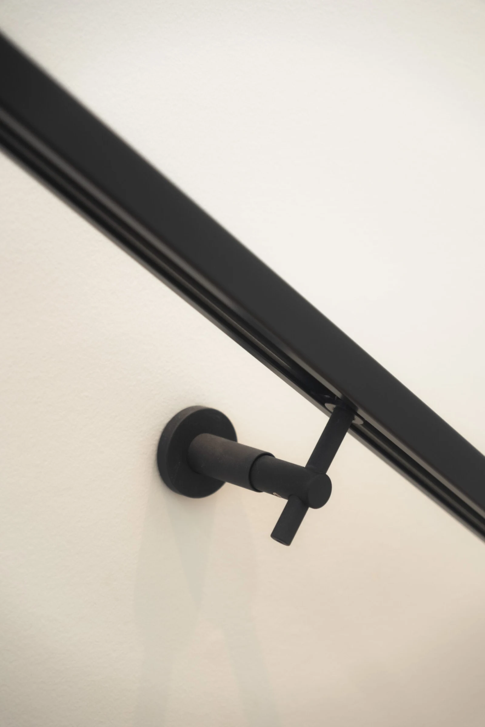 Black handrail returns into a round wall bracket on a plain white wall
