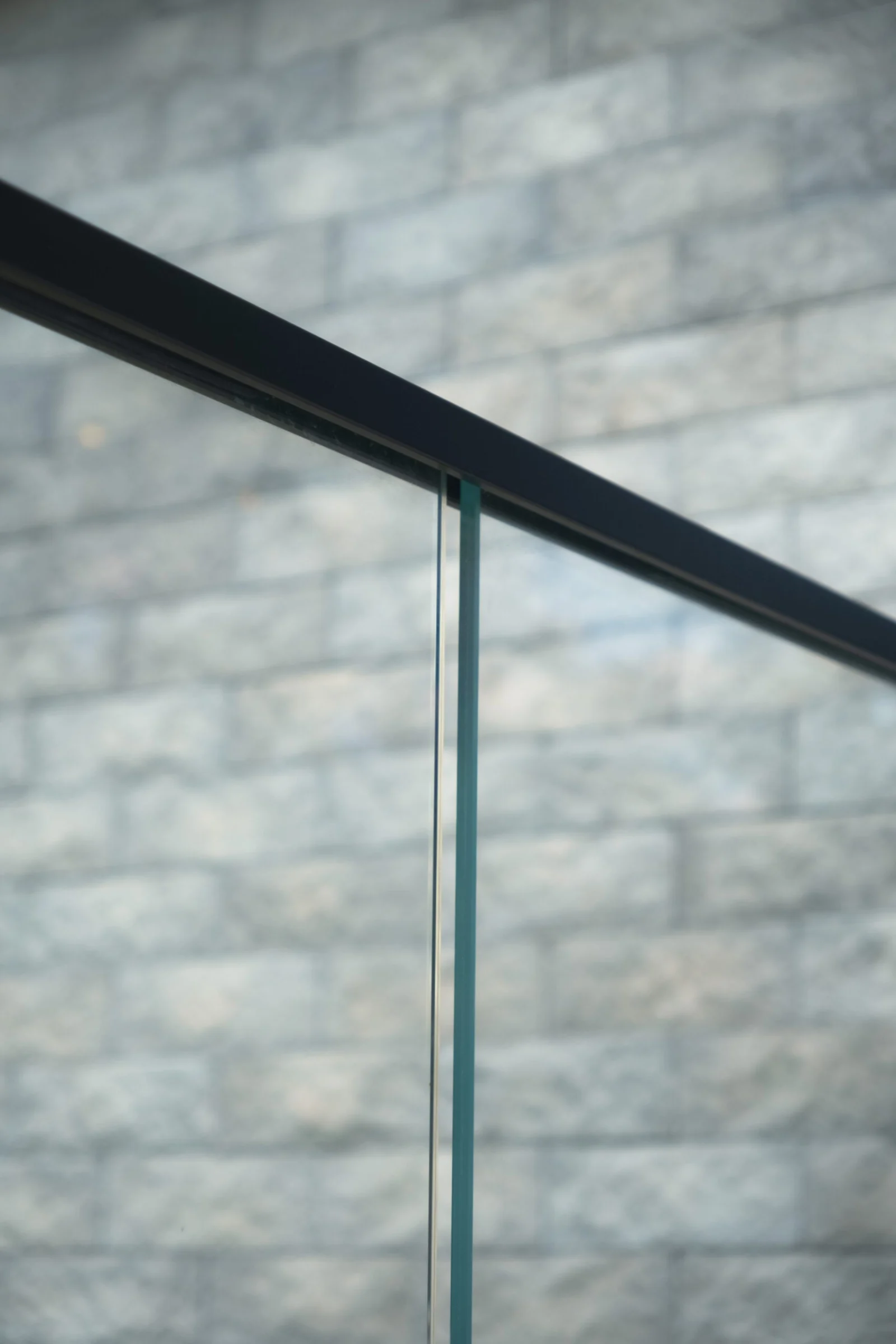 Detail of a black top rail meeting a clear glass panel above stone