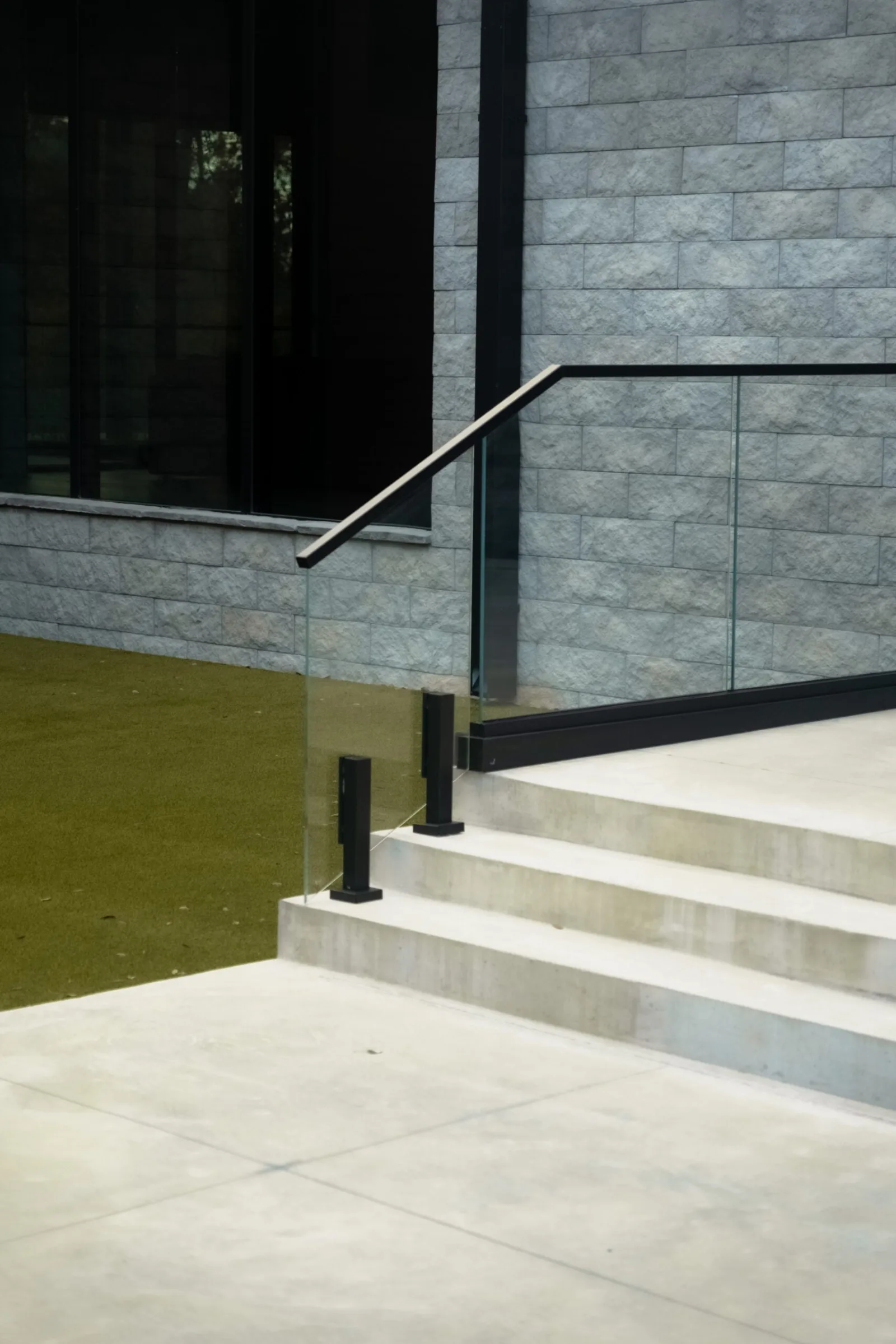 Glass panel on black base shoes beside wide stone entry steps under a gray block wall