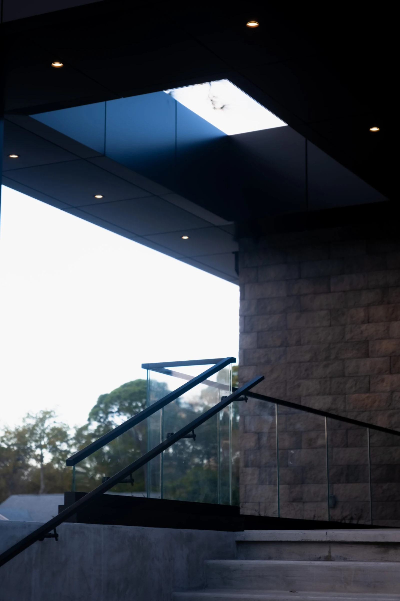 Glass railing with black top rail glows beneath a recessed ceiling skylight