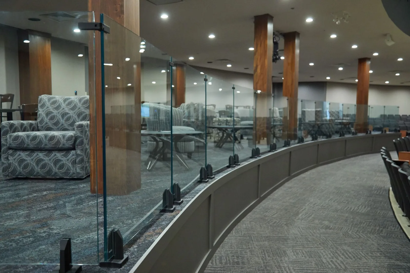 Curved balcony front topped with glass panels on base clamps above carpeted rows of seating