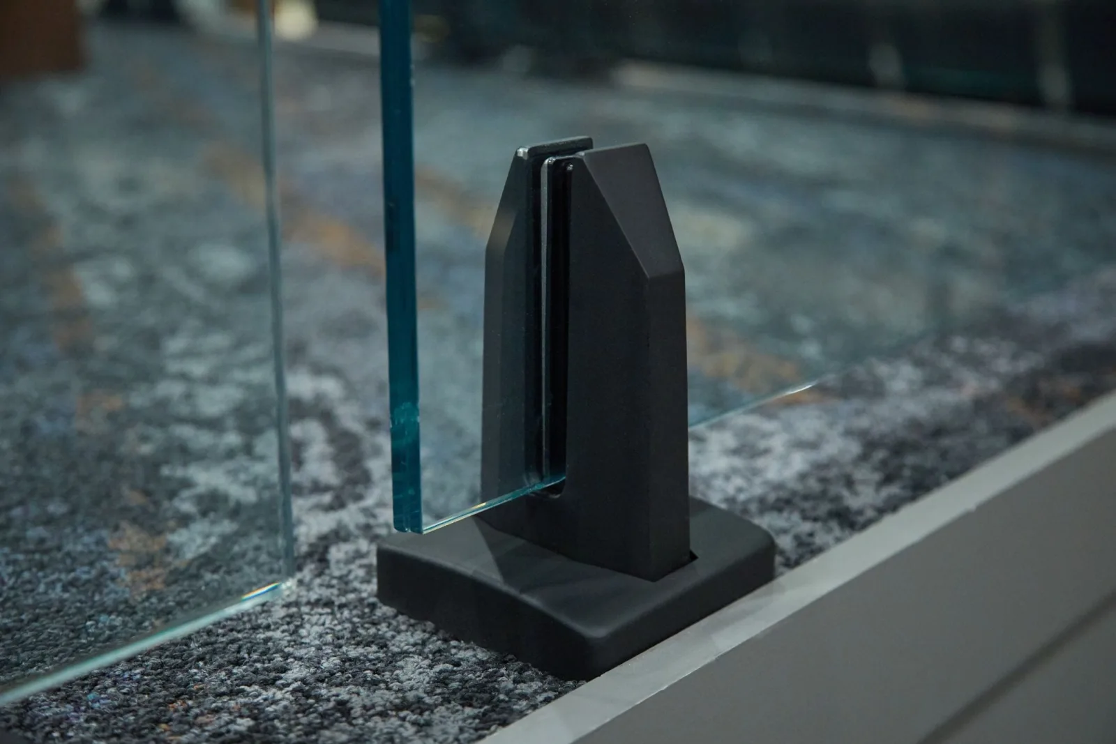 Single black spigot anchoring a glass panel to a polished stone floor edge
