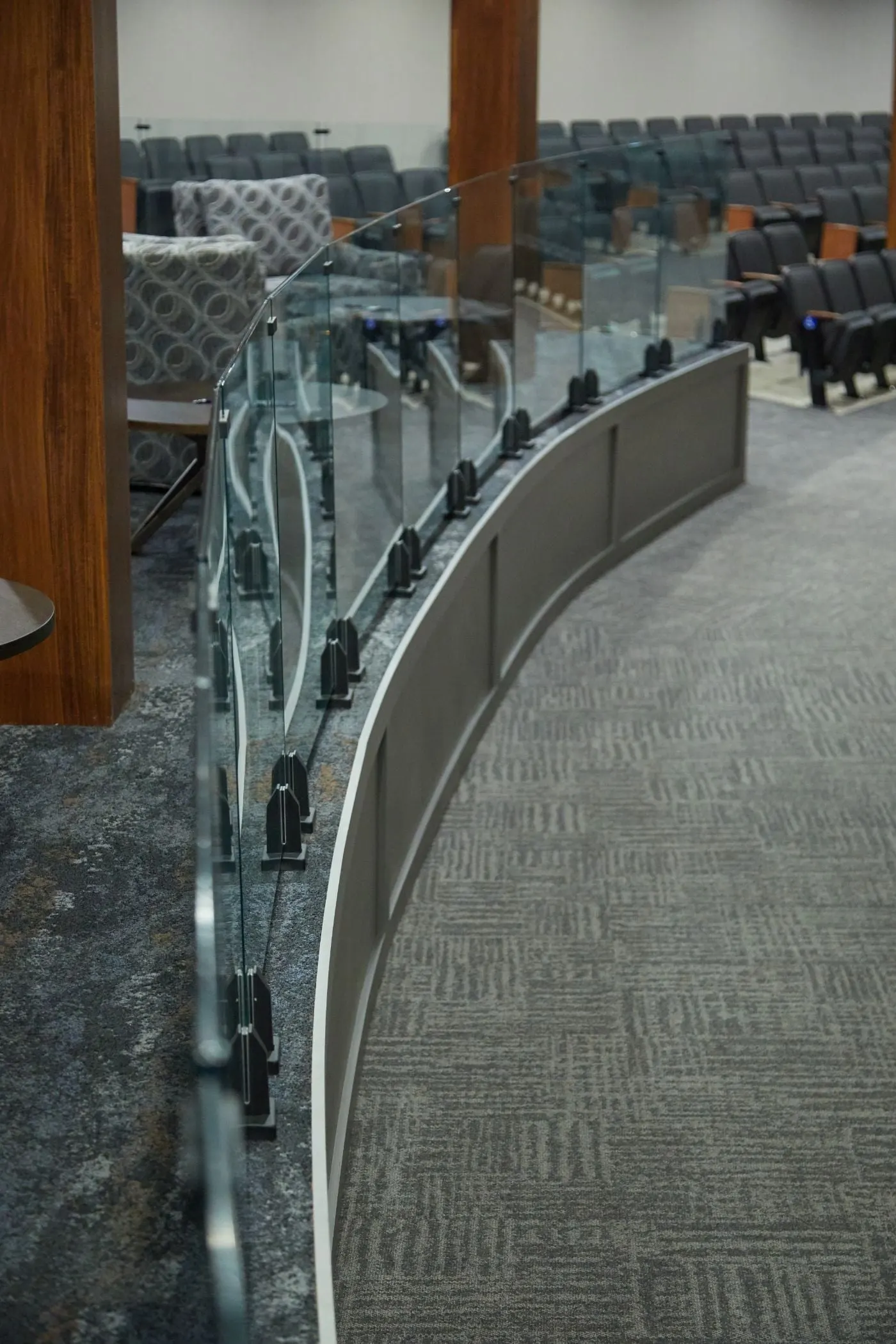 Curved glass railing on black spigots edges a carpeted overlook above auditorium seating