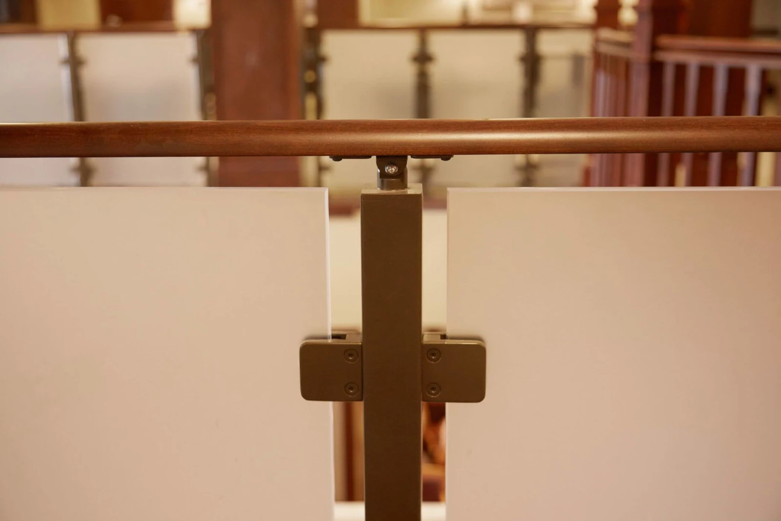 Close view of a bronze clip securing frosted glass under a rounded wood handrail