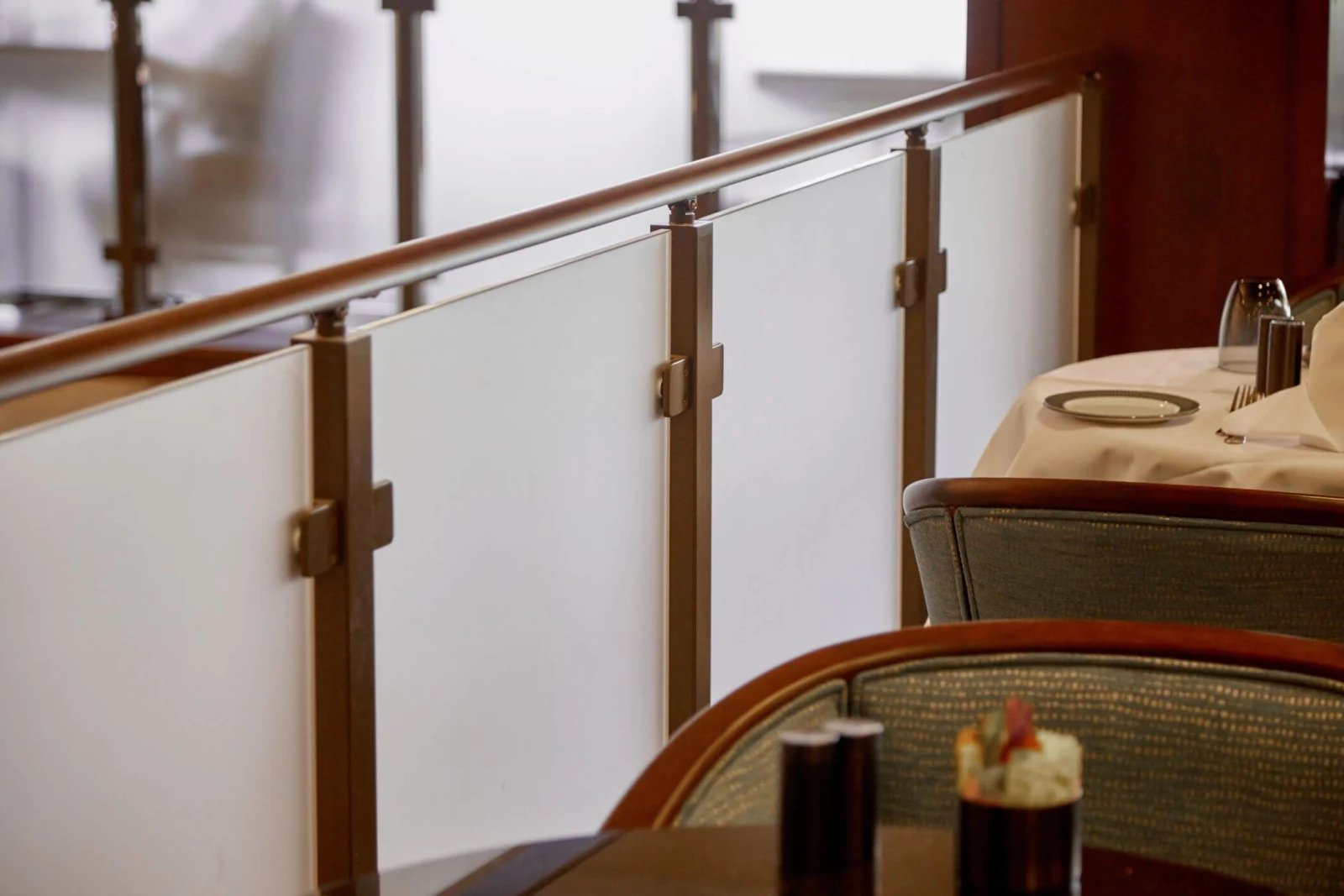 Frosted glass panels with bronze posts and a wood top rail beside dining tables