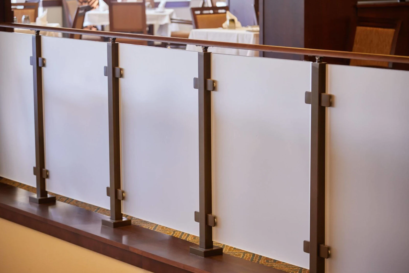 Row of frosted glass infill panels held by bronze clips below a wood rail