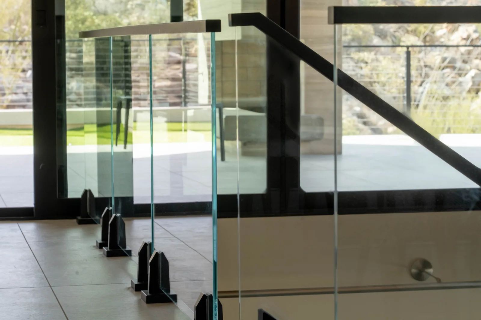 Glass panels on black base clamps at a landing facing tall windows and desert boulders