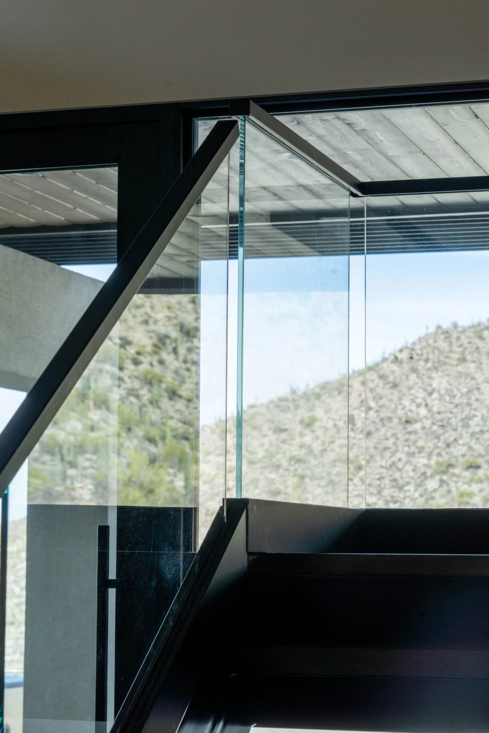 Glass railing at a stair landing framed by dark steel against a rocky slope