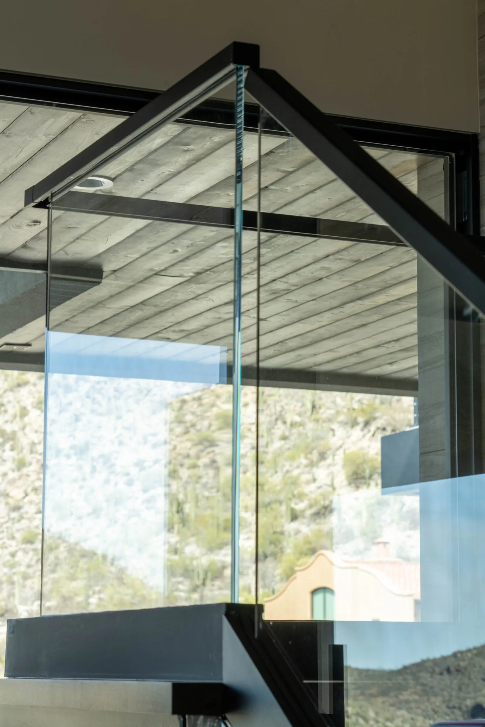 Upper-level glass railing under a plank ceiling with desert hillside filling the windows